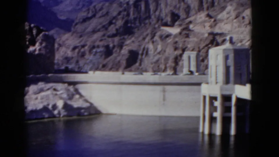 The 1952 California home-movie pan ends with the dam wall, reservoir, rocky backdrop, and pale structures near the right edge.