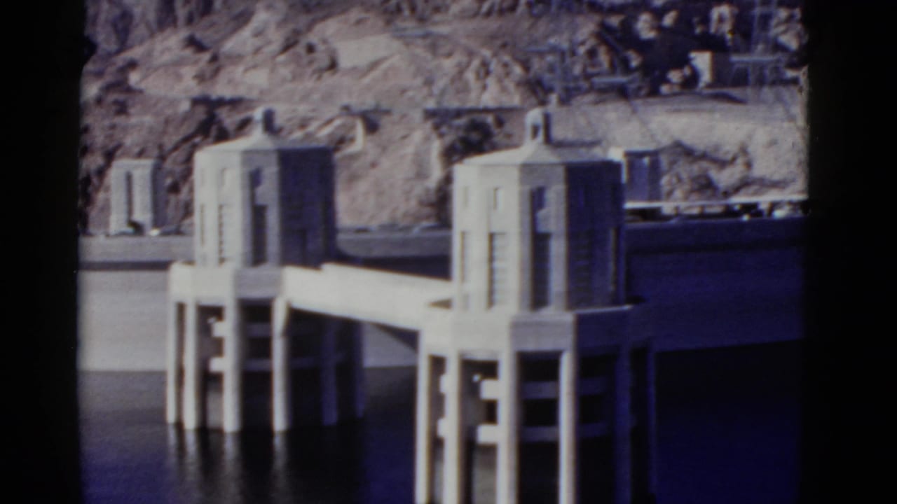 1952 California 8mm frame showing concrete dam intake towers, a deck, vertical supports, reservoir water, and rocky desert terrain.