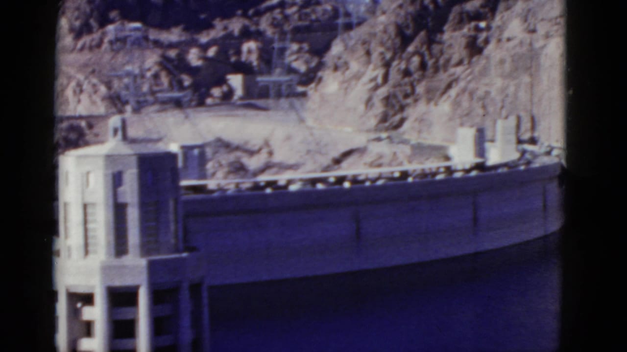 Curved concrete dam and intake structure below grey rocky canyon walls.