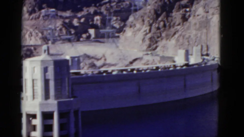 1952 California 8mm frame showing a curved hydro dam section, intake tower, railings, water, and rugged grey rock behind it.