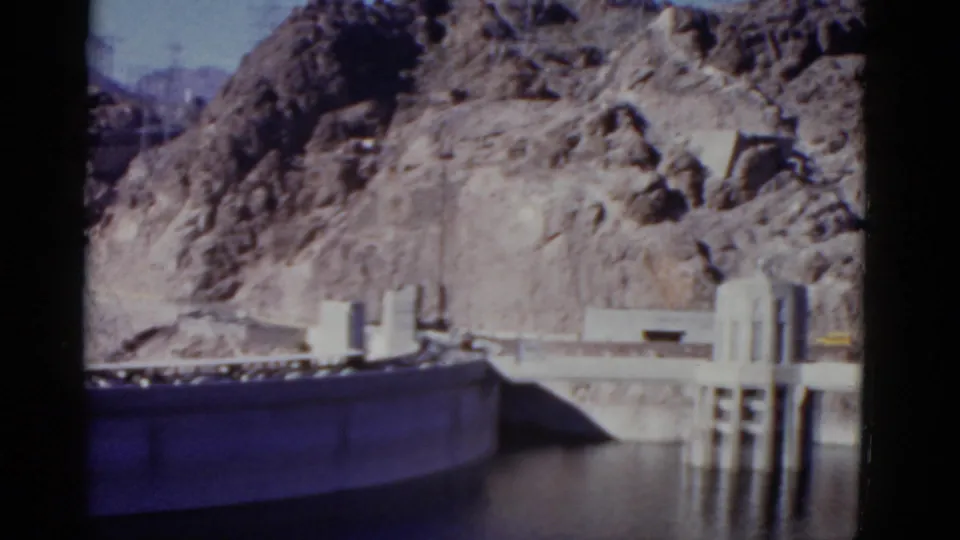 1952 California 8mm frame with dam intake towers rising near the reservoir and a grey canyon wall filling the background.