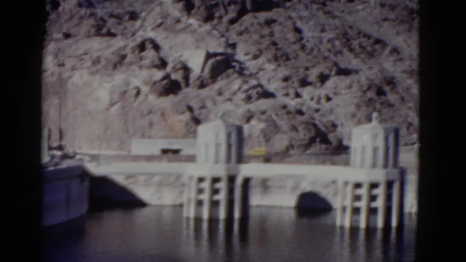 1952 California 8mm frame with intake towers, a concrete dam span, an arched opening, reservoir water, and grey canyon rock.
