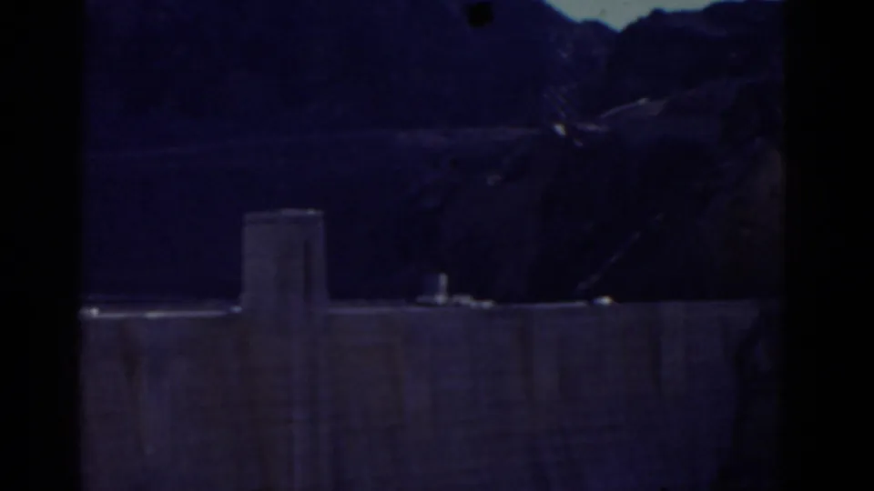 A darker, underexposed frame shows the dam wall, water, and mountainous terrain without the woman clearly visible.