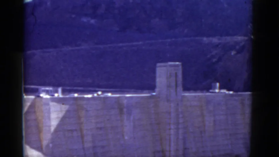 1952 8mm frame showing a closer section of Hoover Dam, including the concrete face, tower form, crest road, and canyon hills.