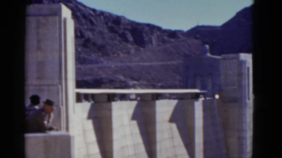 1952 California 8mm frame with two visitors partly visible at a dam overlook beside a concrete tower and mountain backdrop.