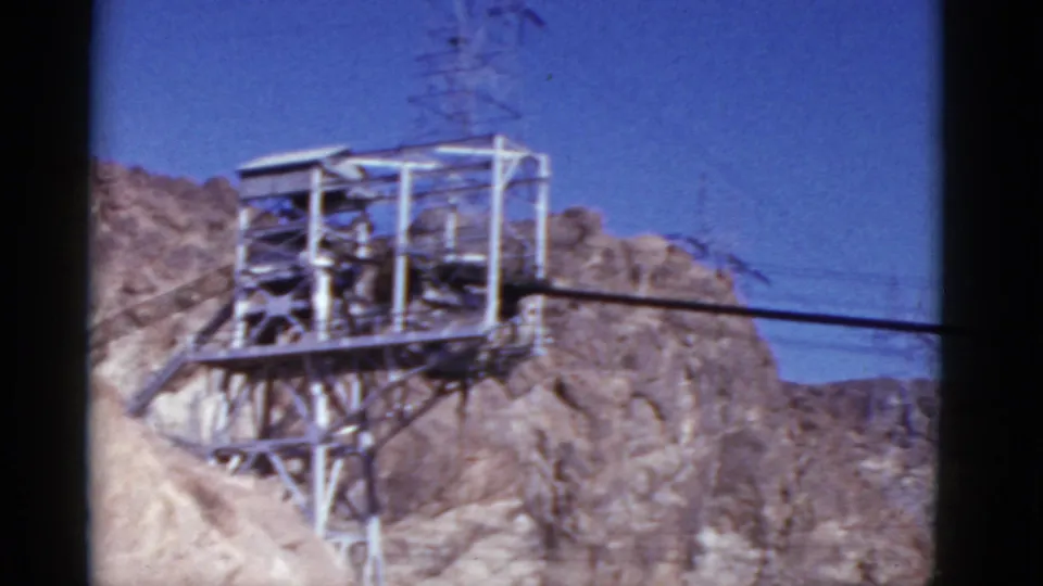 1952 California 8mm frame showing a metal utility structure, power lines, and rugged hillside near the dam setting.
