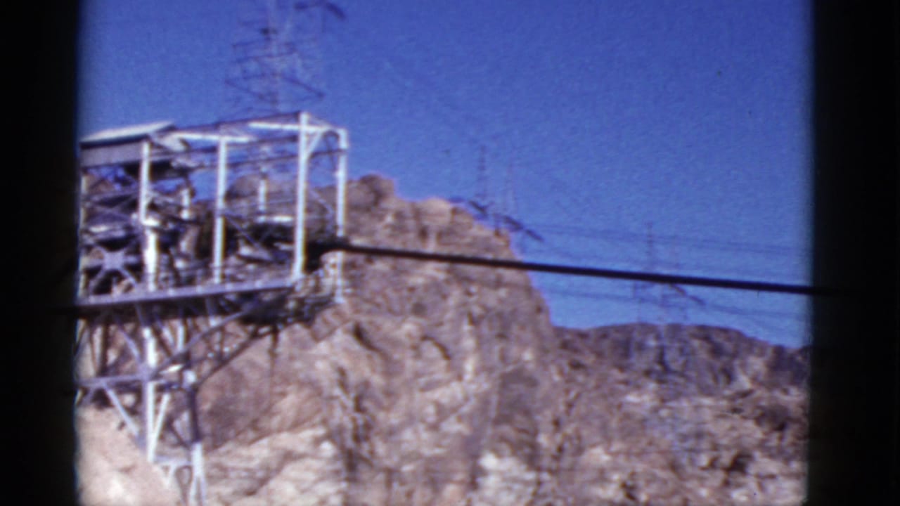 Transmission tower and power lines on rocky mountains beneath a blue sky.