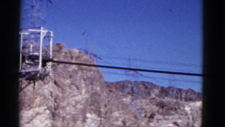 1952 California travel-film view of a mountain ridge, partial transmission tower, and utility lines stretched across blue sky.