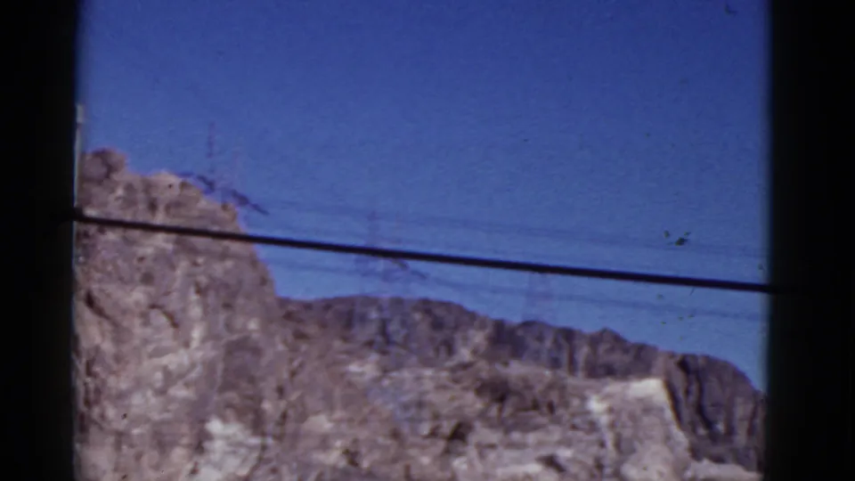 1952 California 8mm frame with arid mountain terrain, distant ridges, and utility lines running across the blue sky.