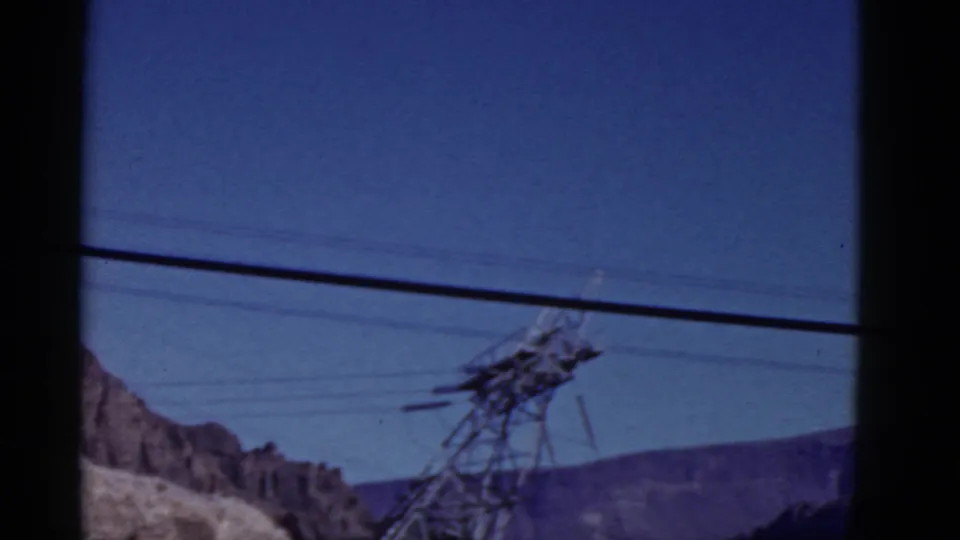 1952 California 8mm frame showing a distant utility tower, power lines, and layered mountain ridges under clear blue sky.
