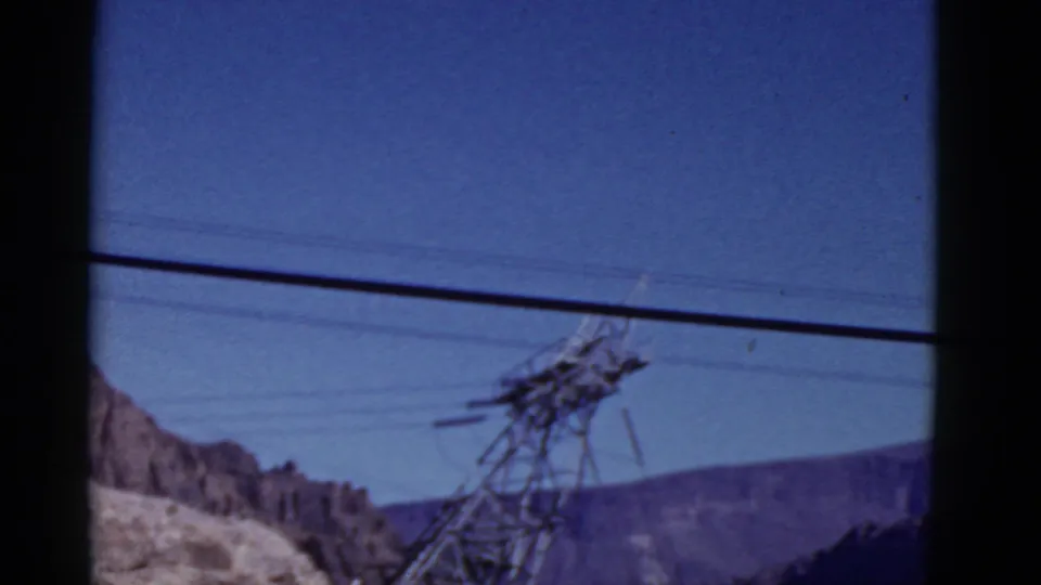 1952 California 8mm frame showing a steel transmission tower, overhead lines, blue sky, and arid mountain slopes from a moving vehicle.