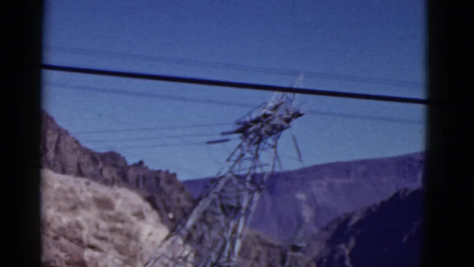 1952 California travel frame with a power pylon crossing the foreground before rugged hills and a deep blue sky.