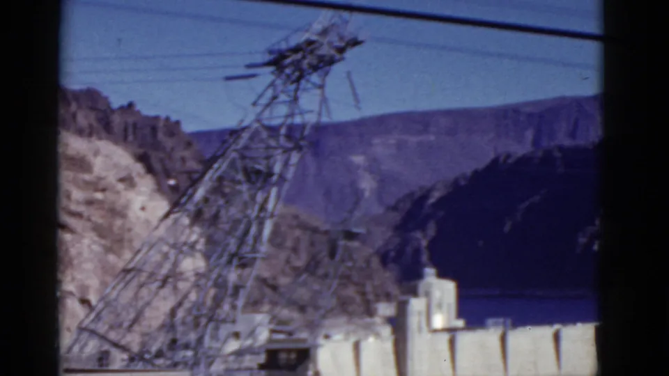 1952 California frame showing a steel power tower, overhead lines, mountains, and pale utility structures at the lower edge.