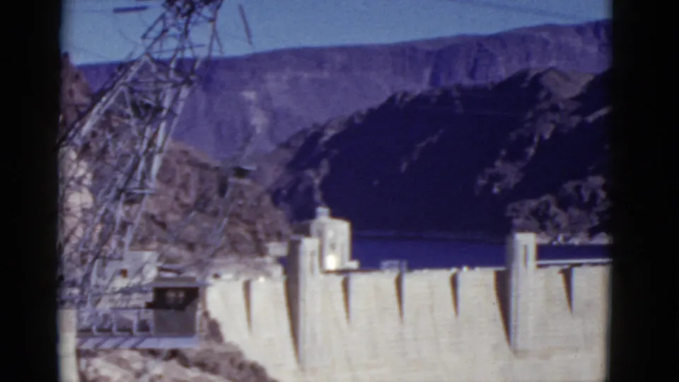 1952 visitor-shot view of Hoover Dam, showing the concrete structure, intake towers, reservoir, and steep canyon slopes.