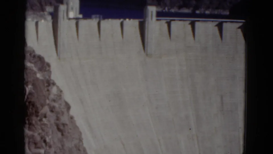 1952 8mm frame holds on the upper Hoover Dam structure, with dark water behind the crest and canyon rock along the left side.