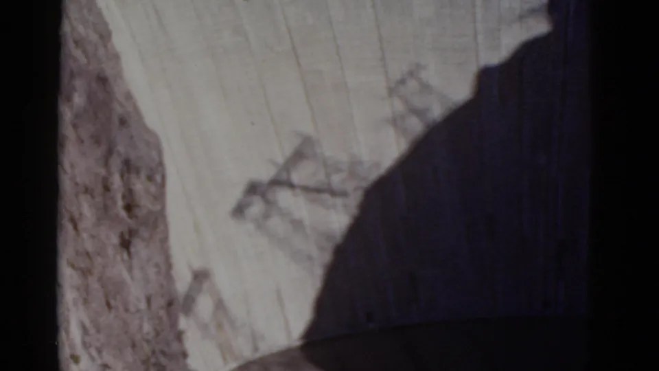 High vantage view of Hoover Dam's curved concrete wall, canyon rock, and deep shadow in faded 1952 home-movie color.