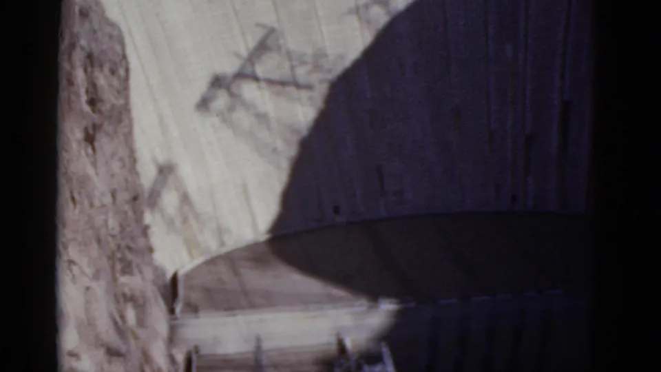 1952 8mm frame showing Hoover Dam's curved face and lower structural details partly obscured by shadow.