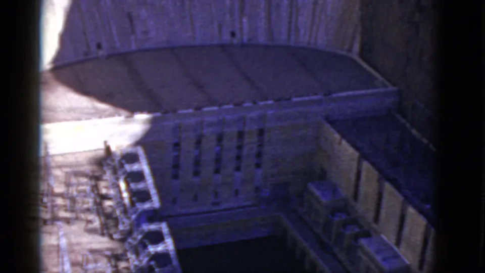 1952 California 8mm frame showing a large stone building courtyard from above, with parked cars, vertical windows, and a dark central open area.