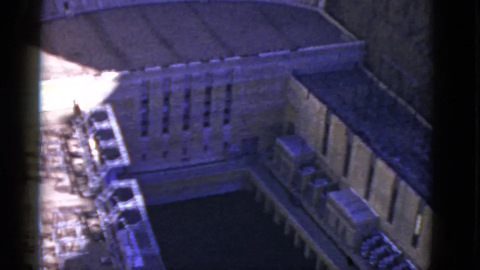 1952 California home-movie frame with a high-angle view into a stone institutional courtyard, including cars along one side and a dark central area.