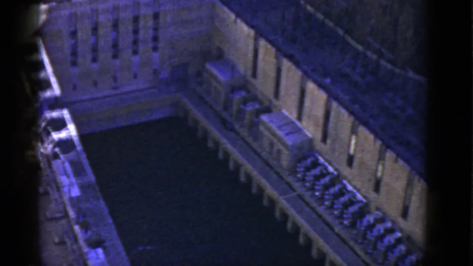 1952 California 8mm frame looking down into an enclosed stone courtyard, with vertical window rows, a dark water-like center, and small structures along the side.