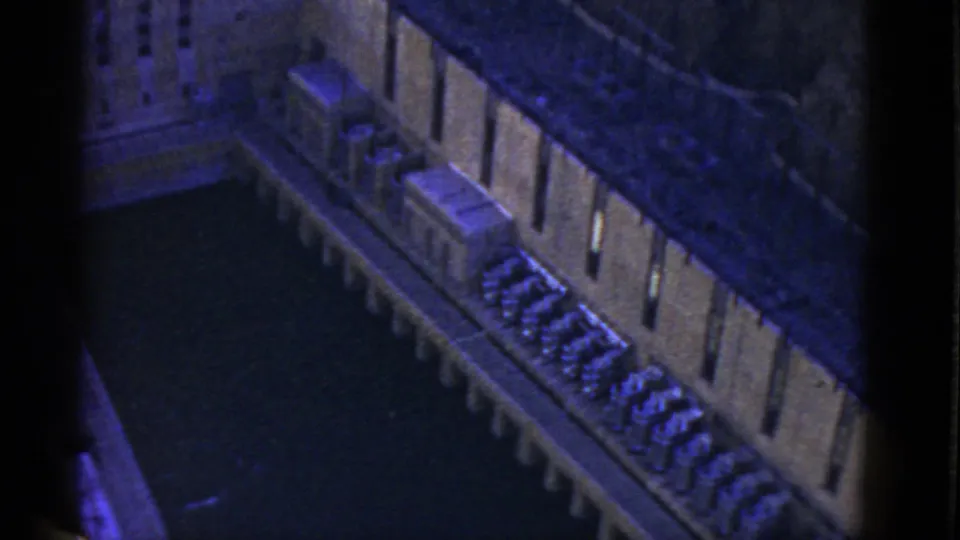 1952 California home-movie frame looking down over a long concrete structure, dark water, and repeated mechanical-looking elements.
