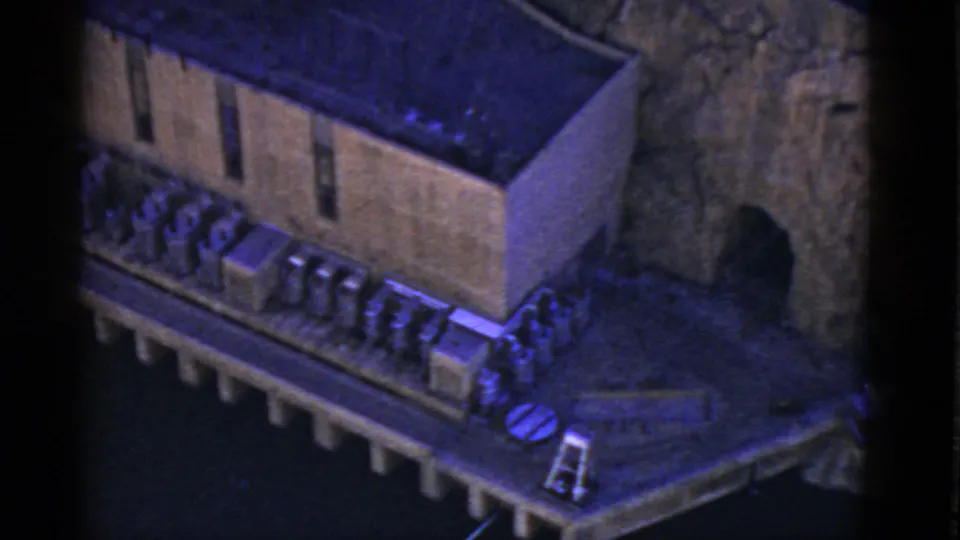 Blue-tinted 8mm frame from California in 1952 showing the side of a concrete structure, exterior units, and adjacent rocky terrain.