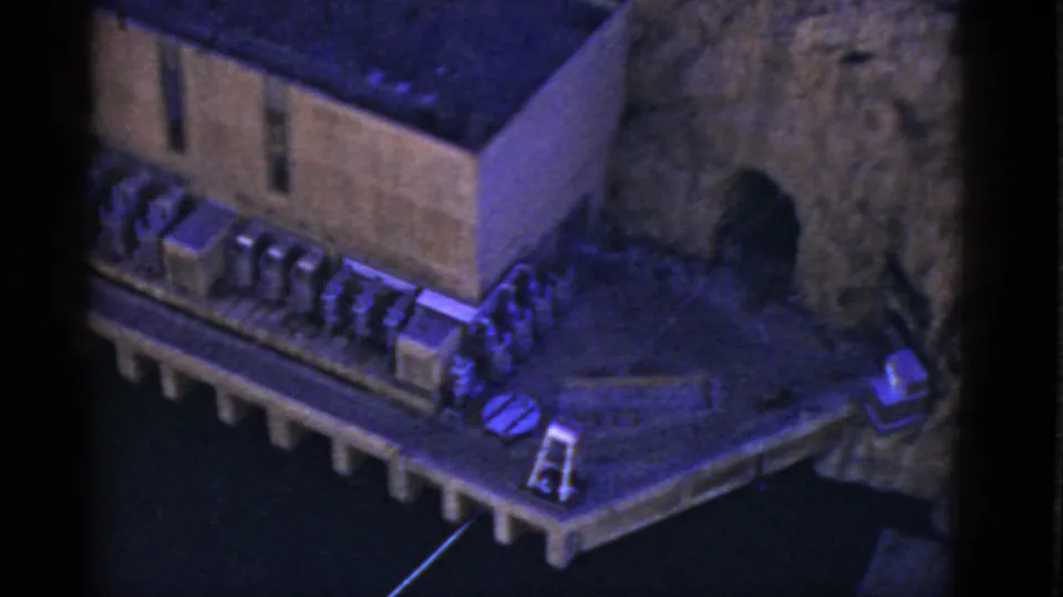 1952 California 8mm frame showing the end of a concrete structure beside a rocky opening, with equipment on a platform over water.