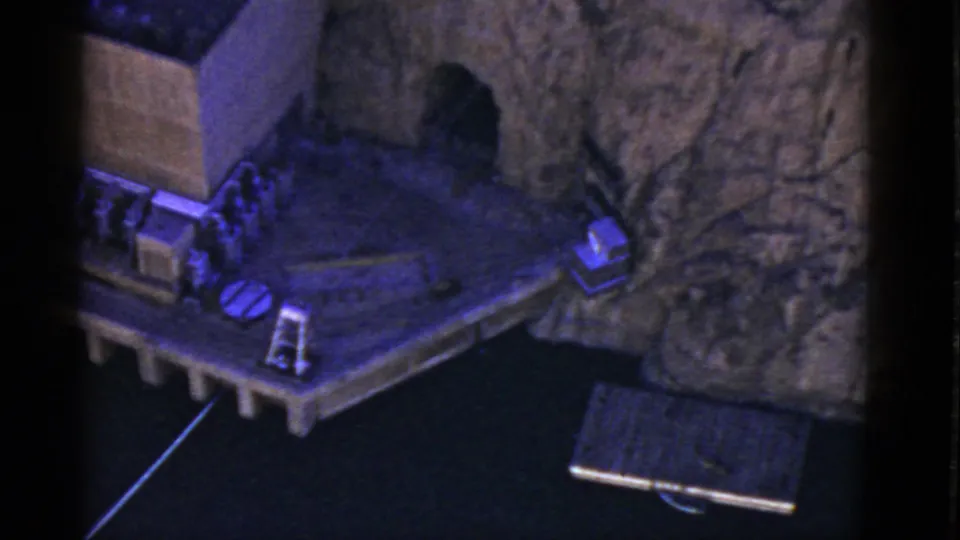 The camera view shifts right across the 1952 California display, showing the platform edge, facade, small objects, and rock-textured background.