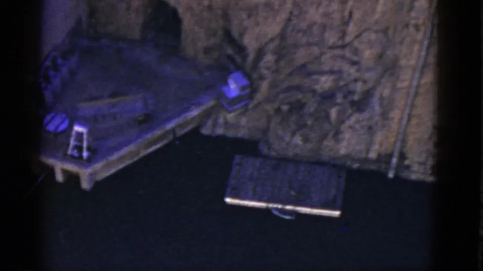 A closer 8mm view of the display emphasizes the platform corner, circular object, small ladder-like piece, and textured scenic backing.