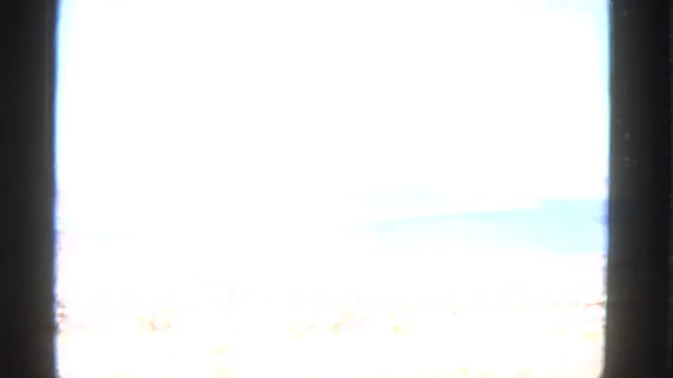 An overexposed 8mm frame appears to look from a dark car interior toward bright outdoor California desert light.