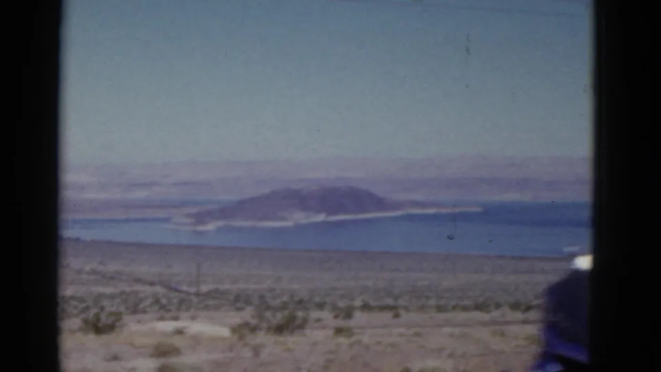 A 1952 California road-trip view shows desert scrub, blue water, and a distant island or low hills under a pale sky.