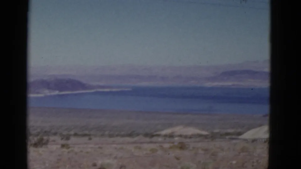 1952 California home-movie view of a desert basin, blue water, pale shoreline, and layered mountains seen from a moving vehicle.
