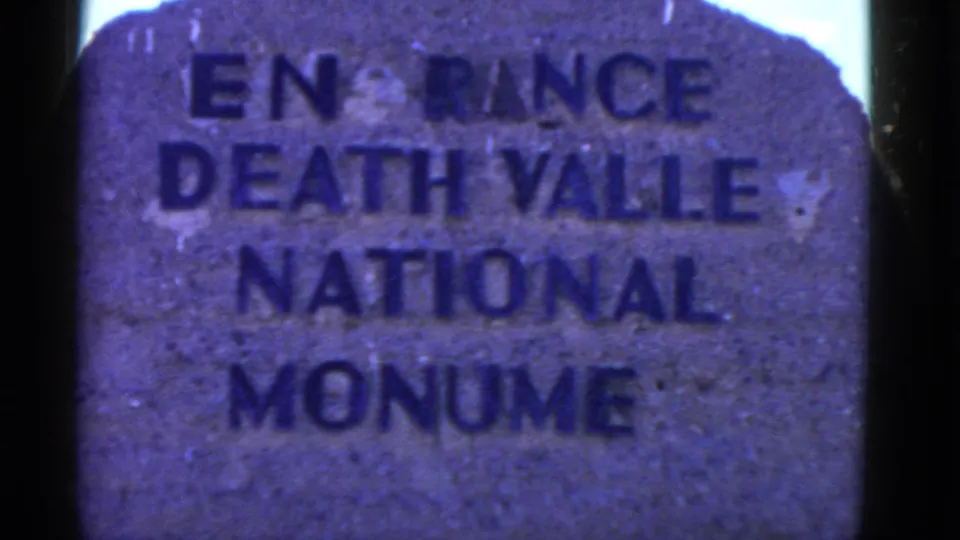 Handheld 8mm view of the Death Valley National Monument entrance marker, cropped tightly with visible film-edge darkness.