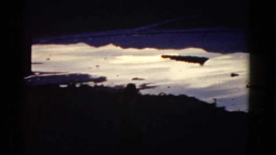 Final 1952 California 8mm frame focusing on bright water, dark shoreline, and distant ridge forms after the sign leaves view.