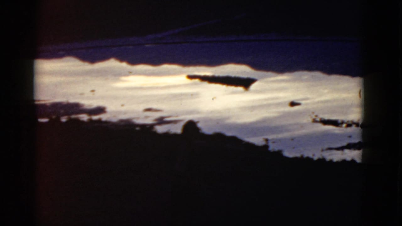 Snowy slope seen through dark foreground silhouettes with a small distant figure near the lower edge.