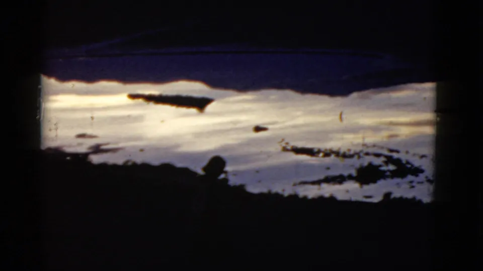 A 1952 California home-movie frame shows a snowy hillside, dark shadowed foreground, and a small human figure near the lower center.
