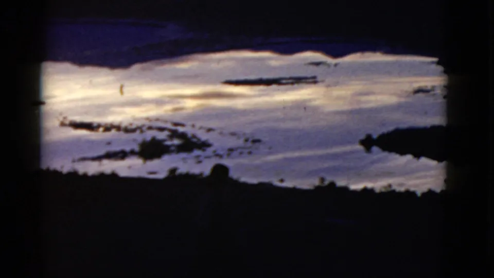 A 1952 California 8mm frame captures a snowy slope, dark foreground shapes, and scattered exposed patches, with a faint human silhouette near the bottom.