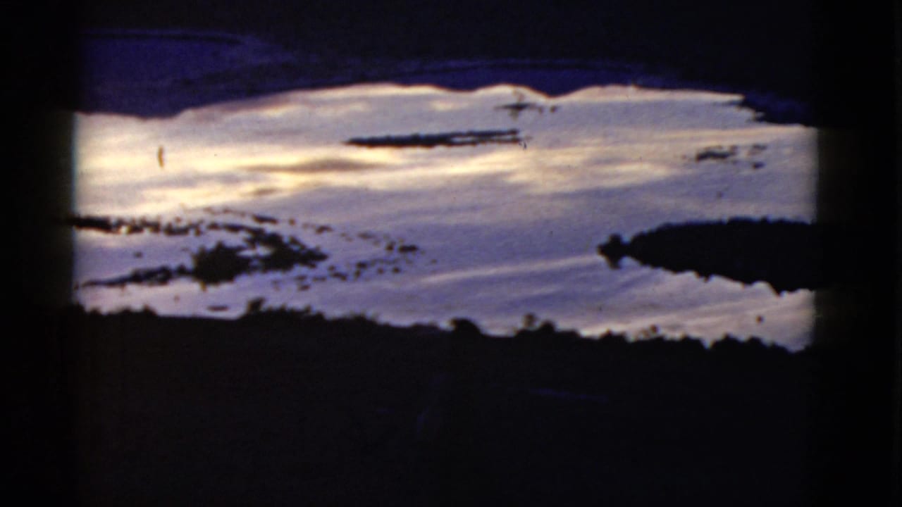 1952 home-movie frame showing reflective coastal water and dark shoreline shapes, likely in California per clip metadata.