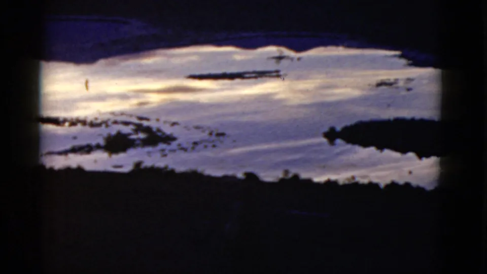 1952 home-movie frame showing reflective coastal water and dark shoreline shapes, likely in California per clip metadata.