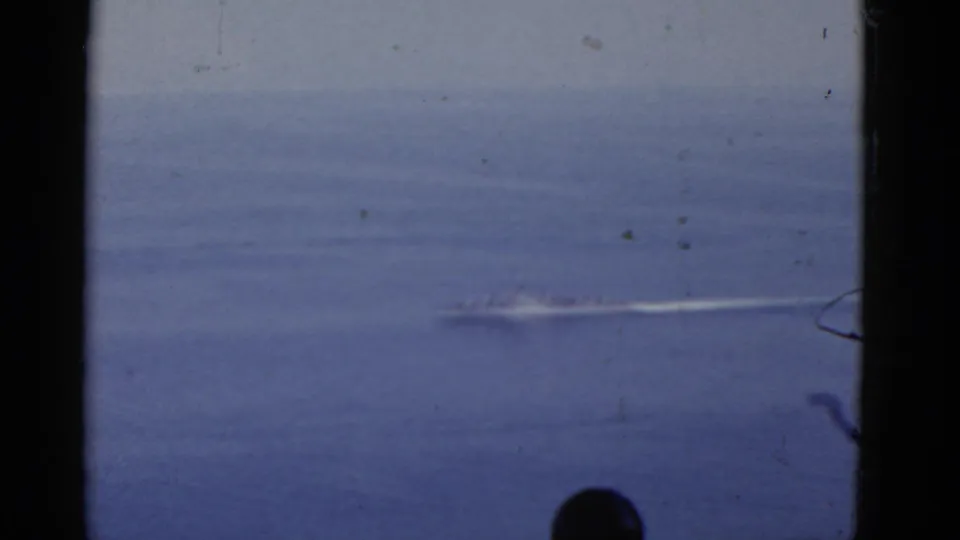 Distant vessel wake crosses open water in a 1952 California home-movie frame, with a partial bystander visible near the lower edge.