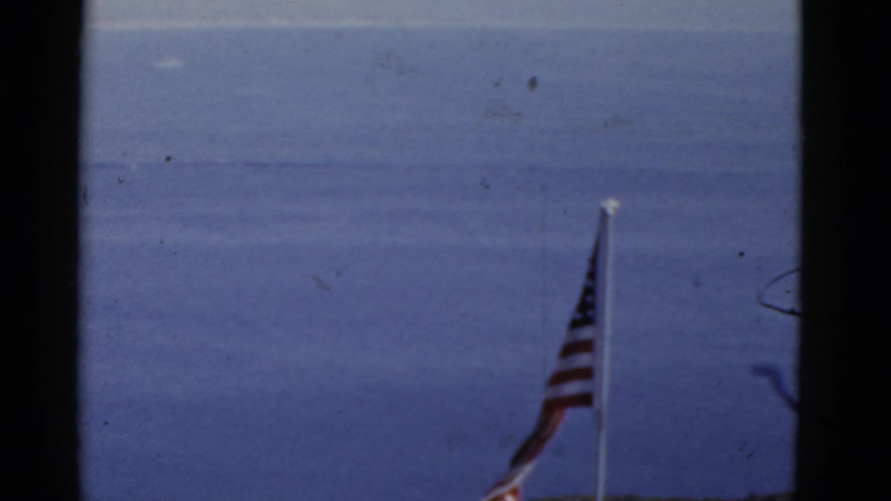 1952 California 8mm frame showing a U.S. flag on a pole against open water and a pale sky.