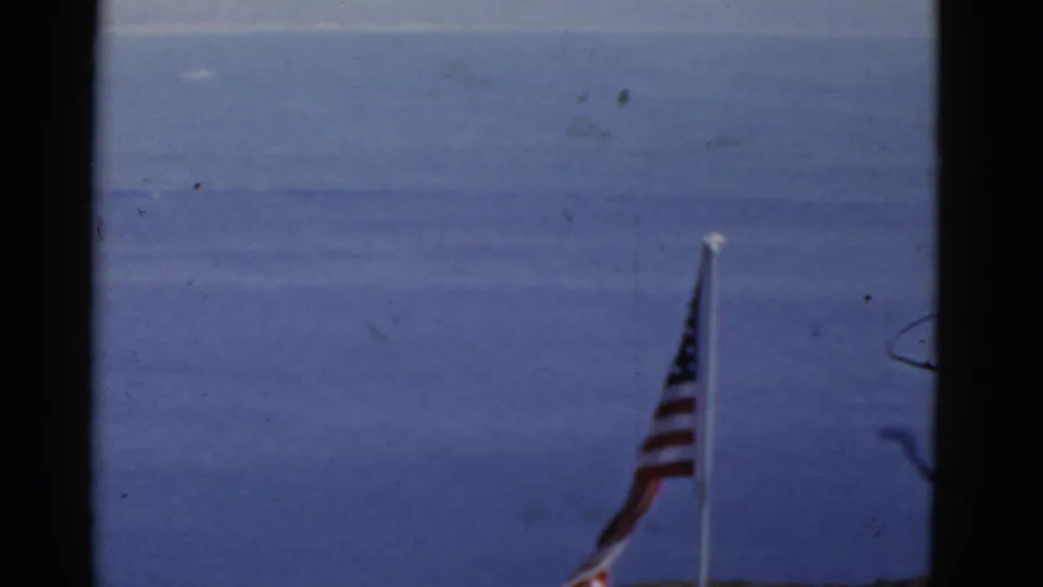 1952 California 8mm frame showing a U.S. flag on a pole against open water and a pale sky.
