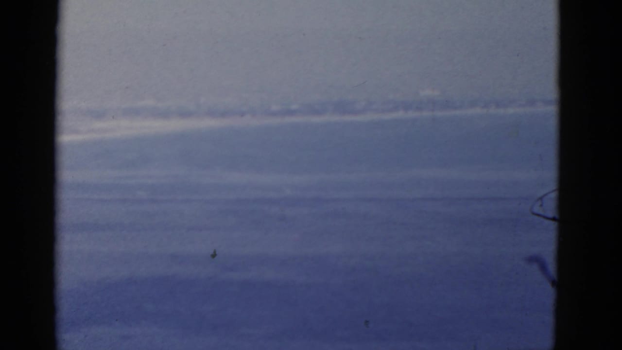 Blue ocean and pale sky seen through dark window trim with a hazy horizon.