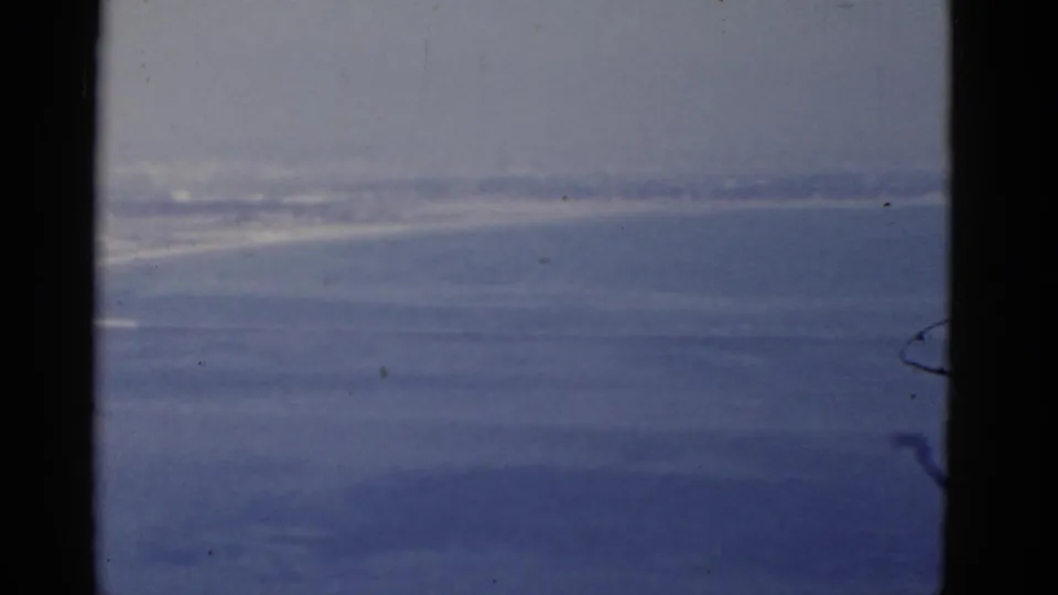 1952 home-movie frame with blue sea, pale sky, and dark window trim along a moving coastal view.