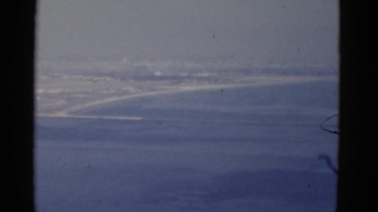 Hazy elevated view over blue ocean toward a pale shoreline and distant coastal development.