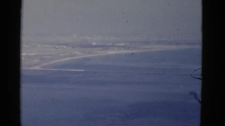 1952 California 8mm frame showing a soft, distant view of ocean, shoreline, and possible harbor landform through haze.
