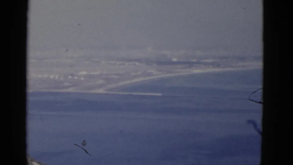 Hazy 1952 California coastal view with ocean in the foreground and a faint harbor or shoreline settlement in the distance.