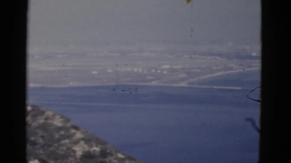 Final 1952 California frame shows a soft ocean view, distant coastal buildings, and a rocky foreground edge within visible 8mm borders.