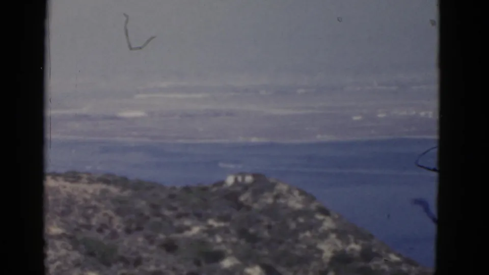 1952 California 8mm frame looking across a dry hillside toward bay water and an indistinct far shore.