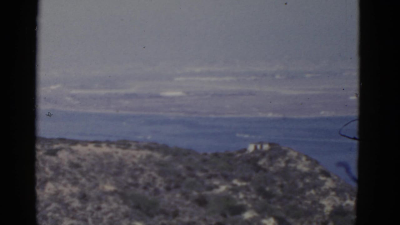 1952 California home-movie frame showing scrubby coastal hills and a distant blue ocean horizon through soft 8mm grain.